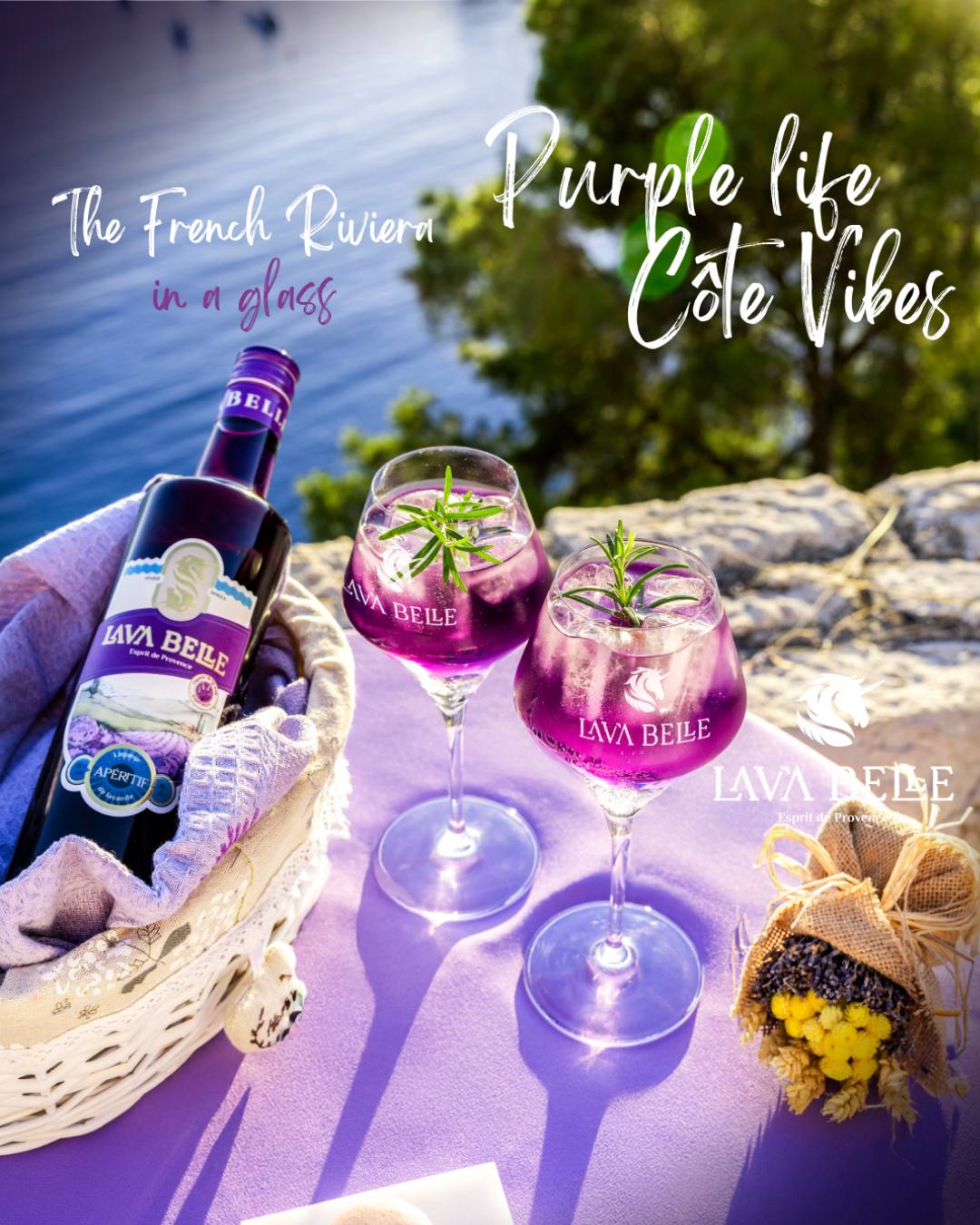 Two glasses of Lav'a Belle Spritz and a bottle in a picnic basket by the sea, lettering The French Riviera in a glass